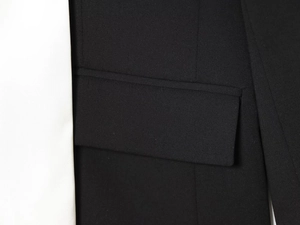 Detailed close-up of the black blazer fabric texture and refined flap pocket design