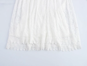 Détail de la broderie en dentelle florale blanche sur l'ourlet de la robe longue