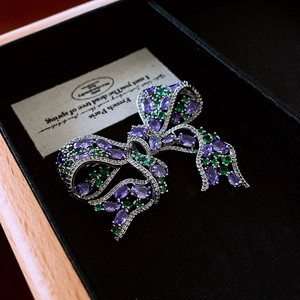 Detail shot of vintage bow brooch with purple and green zircons on a black velvet box