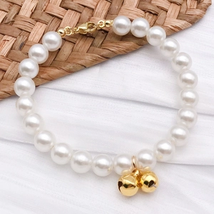 Detail of white pearl bracelet with gold metal clasp and jingling bell charms on mat
