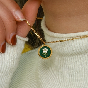 Close-up of 18K gold plated necklace with a green enamel daisy flower pendant on a model