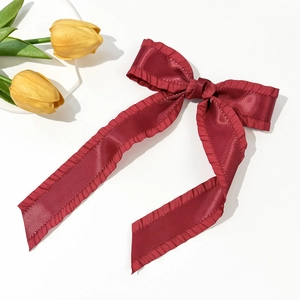 Deep red satin bow hair clip with ruffle edges on a white surface with yellow tulips