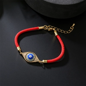 Macro detail of red woven bracelet with gold evil eye charm and zircon stones