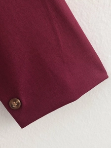 Detail of burgundy twill jacket sleeve featuring a round brown button closure