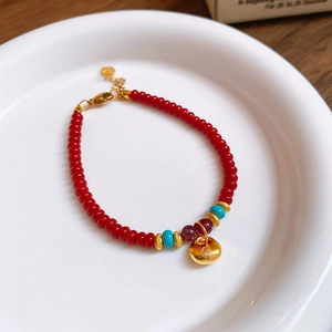 Détail macro du bracelet en perles rouges avec pierres turquoise et breloque dorée Fu