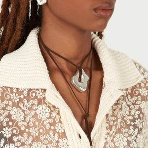 Close-up of irregular silver pendant with brown cord and stud earrings on model