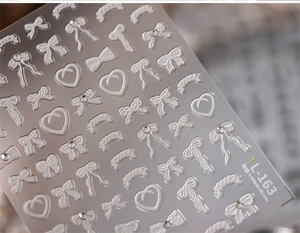 Macro shot of 3D embossed white bow and heart nail art stickers with rhinestones