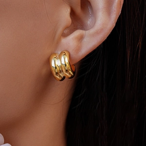 Close-up of golden triple-layered C-shaped stud earrings worn on the ear model