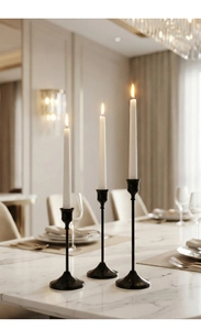 Juego de tres candelabros de metal negro mate con velas blancas encendidas en mesa de mármol
