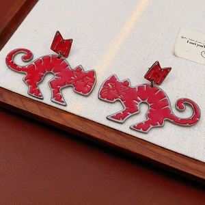 Detailed close-up of red enamel crown cat earrings with bow accents on wooden tray