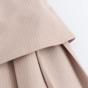 Close-up detail of beige pinstripe pleated fabric texture on a preppy style dress