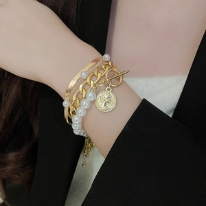 Close-up of layered gold chains with snake links, round pendant, and pearl beads