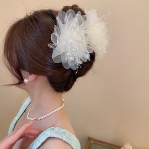 Detail view of a large white tulle flower hair claw with pearl tassels on a model