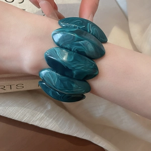 Detail view of emerald green marble texture acrylic bracelet on a wrist against soft fabric