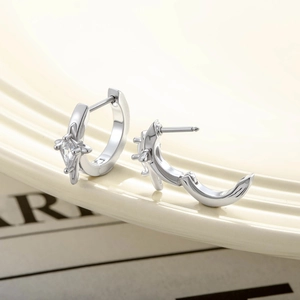 Silver star and moon earrings with micro-inlaid zircons on a beige ceramic plate