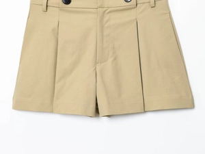 Dettaglio dei pantaloncini kaki a pieghe con bottoni neri e trama in twill di qualità