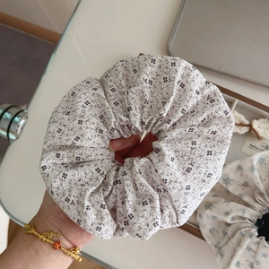 Detailed view of a large cream floral scrunchie with purple patterns worn on a wrist