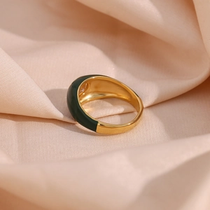 Close-up of gold-plated ring with green enamel finish on soft beige silk background