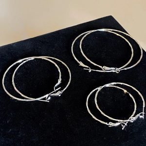 Three pairs of twisted silver hoop earrings in small, medium, and large sizes on black velvet