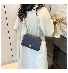 Detail of dark blue denim crossbody bag featuring quilted patterns and gold chain strap