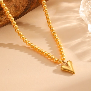 Detail of golden beaded necklace with a 3D heart pendant on a warm beige background