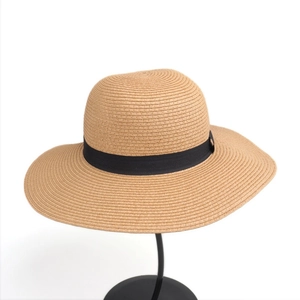 Detail of a beige wide-brim straw sun hat featuring a black grosgrain ribbon on a display stand