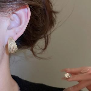 Detailed close-up of a gold-plated multi-layered C-shaped metal earring with striped texture