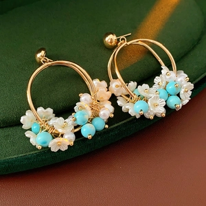 Detail of gold hoop earrings with white flower beads and blue pearls on green velvet
