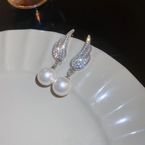 Close-up of silver wing earrings with sparkling crystals and white pearls on ceramic