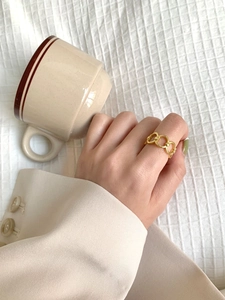 Detail of a gold chain link ring worn by a model holding a cup on white fabric
