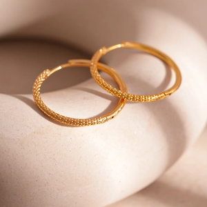 Close-up of golden geometric hoop earrings featuring intricate hammered metal texture