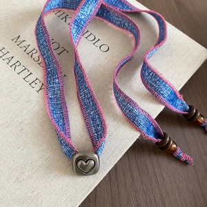 Detailed close-up of blue denim heart pendant necklace with pink stitching and metal slider