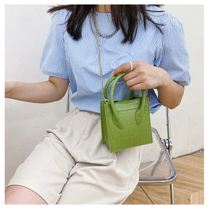 Green faux-crocodile small square bag with chain strap held by model in casual outfit