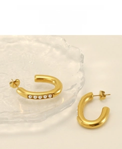 Close-up of gold chunky C-shaped earrings with five white pearls on a glass tray