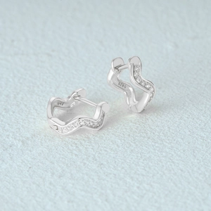 Macro detail of wave-shaped S925 sterling silver earrings with inlaid zircon crystals
