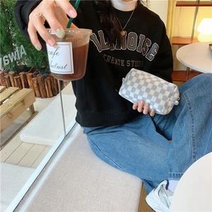 Lifestyle shot of blue and white checkered knit pouch held by a model in a cozy cafe setting