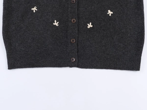 Detailed view of charcoal gray knit cardigan featuring embroidery bows and wooden buttons