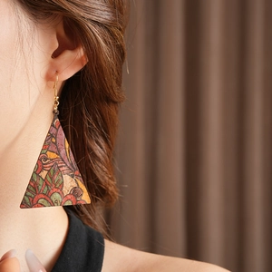 Detail view of triangular leather earrings with vintage ethnic patterns worn by a model