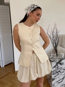 Détail d'un ensemble gilet sans manches boutonné et jupe boule crème en tissu texturé chic