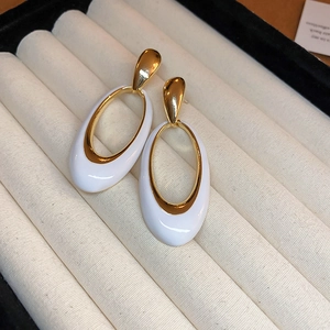 Macro shot of vintage oval gold-tone earrings with white enamel on a striped tray