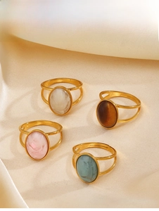 Detail of four retro gold rings with oval resin stones on soft beige satin fabric