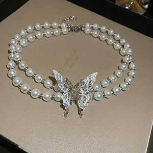 Detail of double-layer pearl necklace featuring a large glittery butterfly pendant on a display box