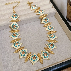 Detail of vintage gold necklace with white enamel, blue patterns, and amber gemstone center