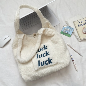 Detail of plush cream fleece tote bag featuring blue luck luck luck letter embroidery
