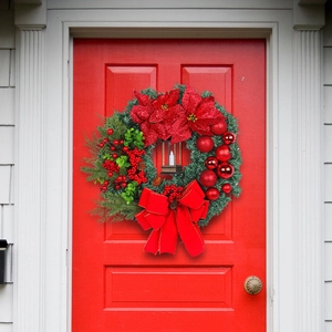 Christmas wreath with red poinsettia, pine cones and lantern on a red door background