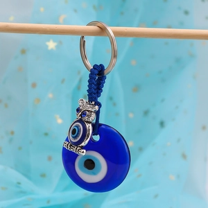Detail of blue evil eye keychain with silver owl charm and braided cord on wood branch
