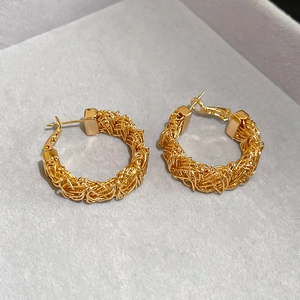 Macro shot of gold-plated woven texture C-shape hoop earrings on a velvet display stand