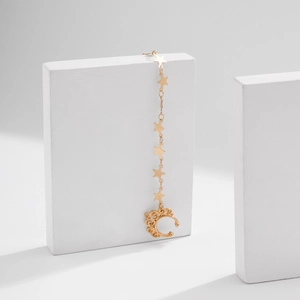 Detail of gold ear cuff with star charms and chain on a white geometric prop