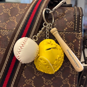 Detailed view of mini baseball, yellow glove and wooden bat keychain on a brown leather bag