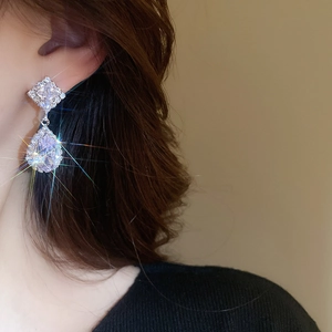 Macro shot of silver teardrop and square zircon earrings with brilliant sparkling effect